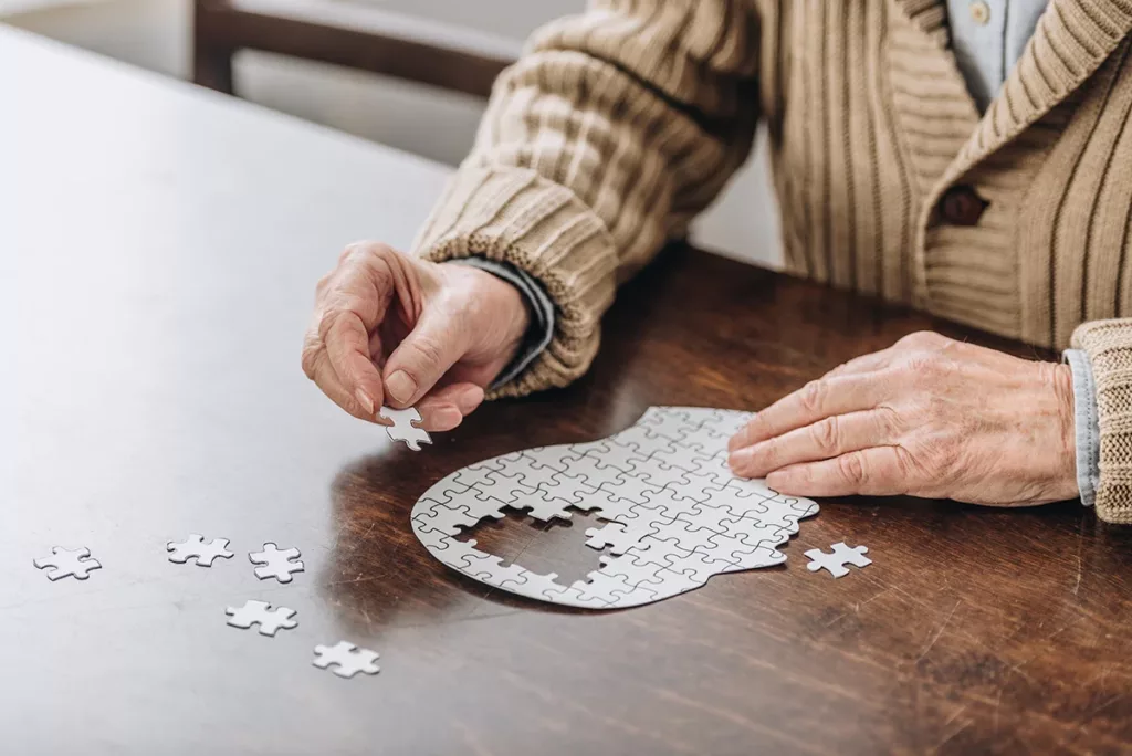 cropped view of senior man doing a puzzle shaped like a head, symbolizing hearing loss and dementia